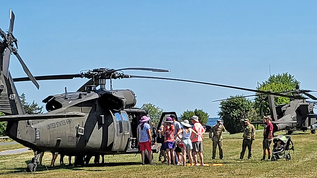 Photo of US Army helicopters displayed by the 10th Mountain Division at the Sackets Harbor Battlefield State Historic Site being visited by members of the public at the Can-Am Festival