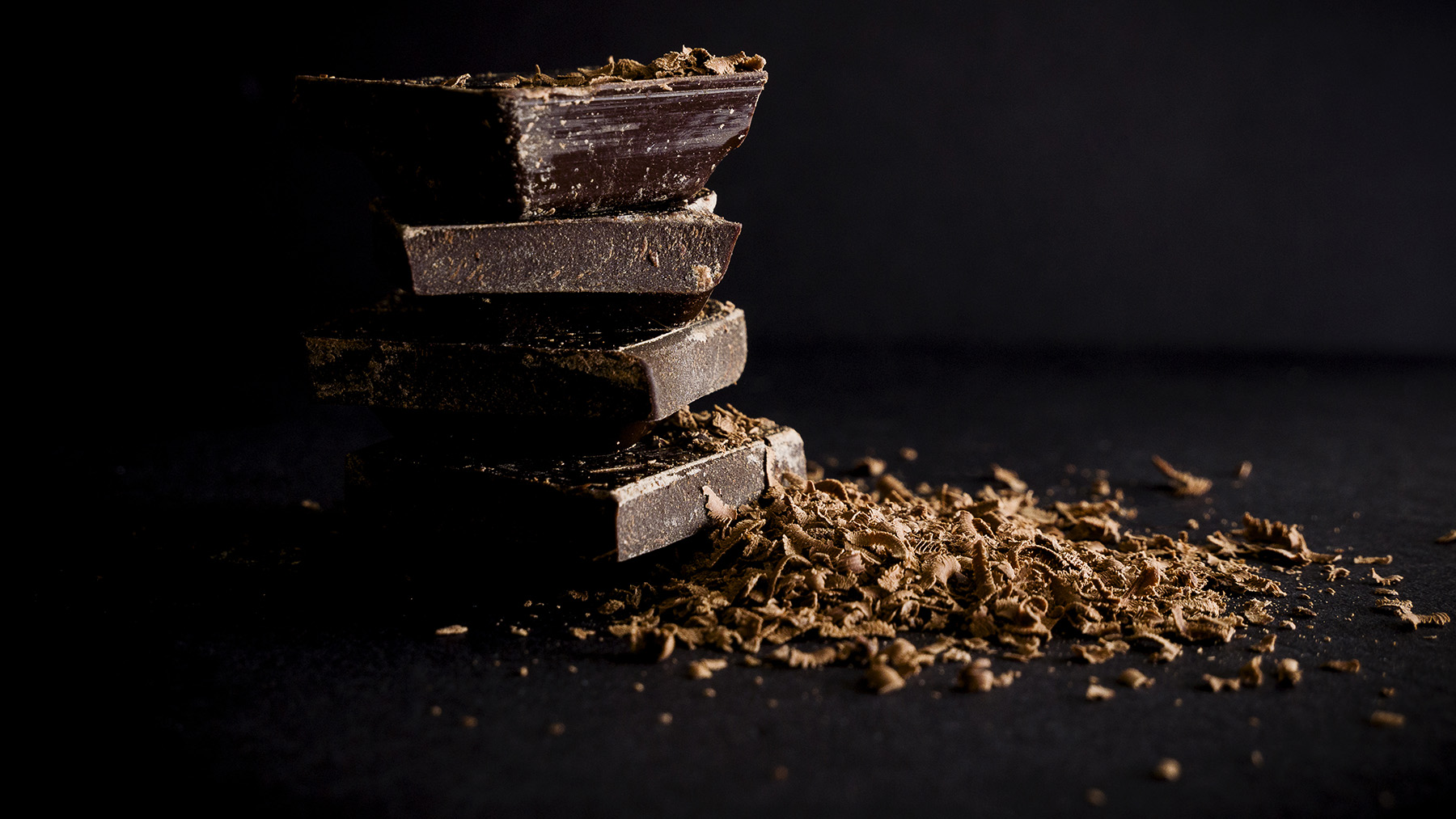 Photo of several small bars of chocolate and chocolate shavings on a dark background (Image from Wikimedia Commons, courtesy of RawPixel.com)