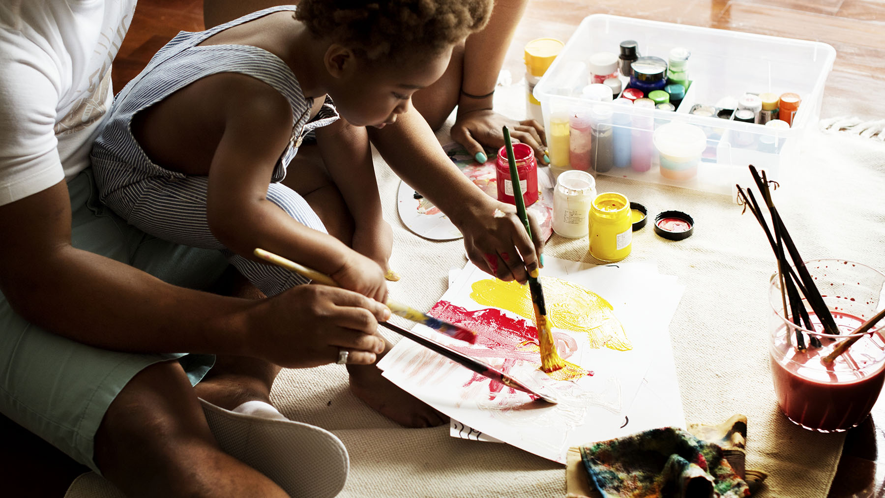 Stock photo of a black child painting with adults in background (Image from RawPixel.com)