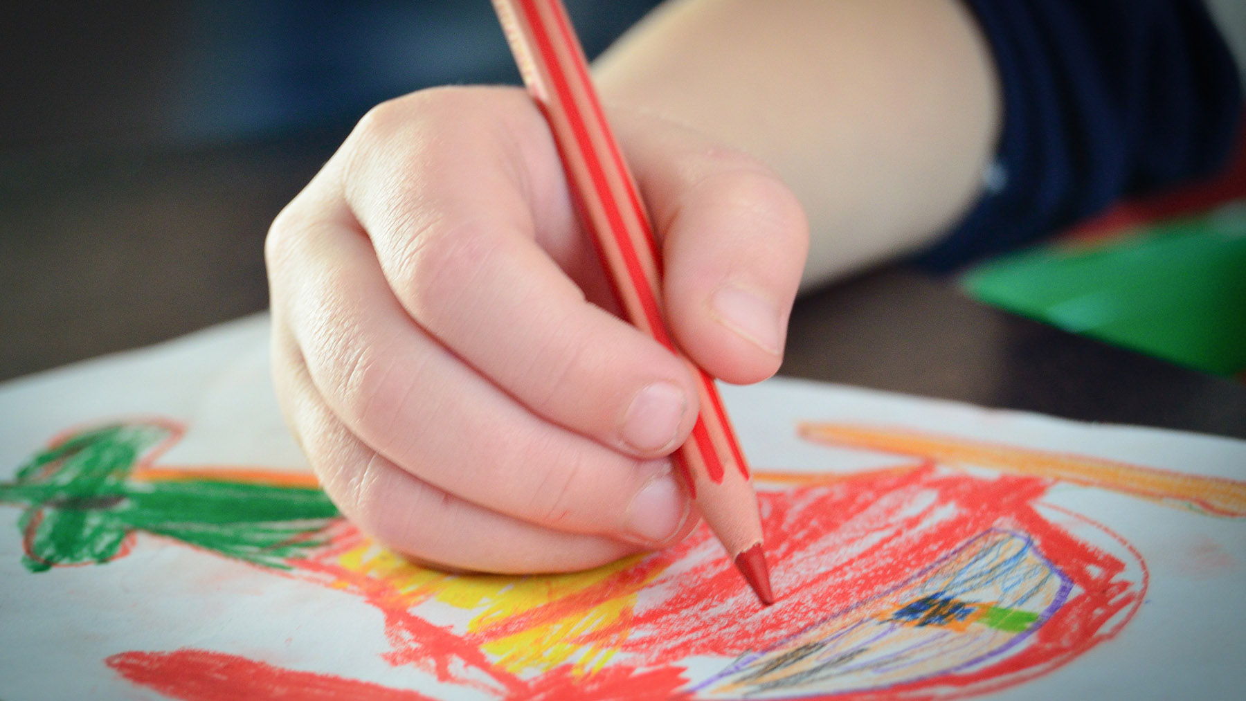 Photo of a child drawing a picture with colored pencils on paper (Creative Commons image, courtesy of RawPixel.com)