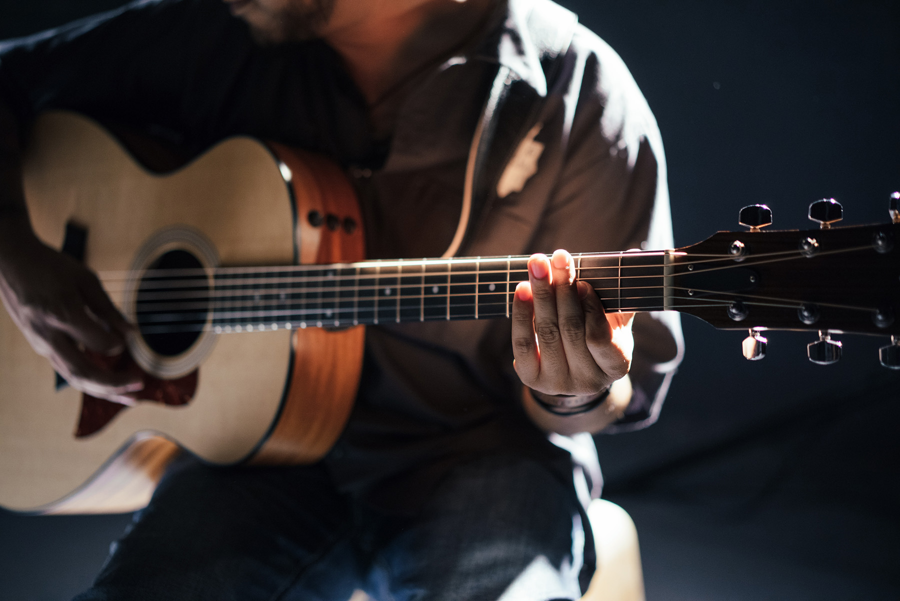 Stock photo of a seated person playing acoustic guitar (Image from Wikimedia Commons, courtesy of RawPixel.com)