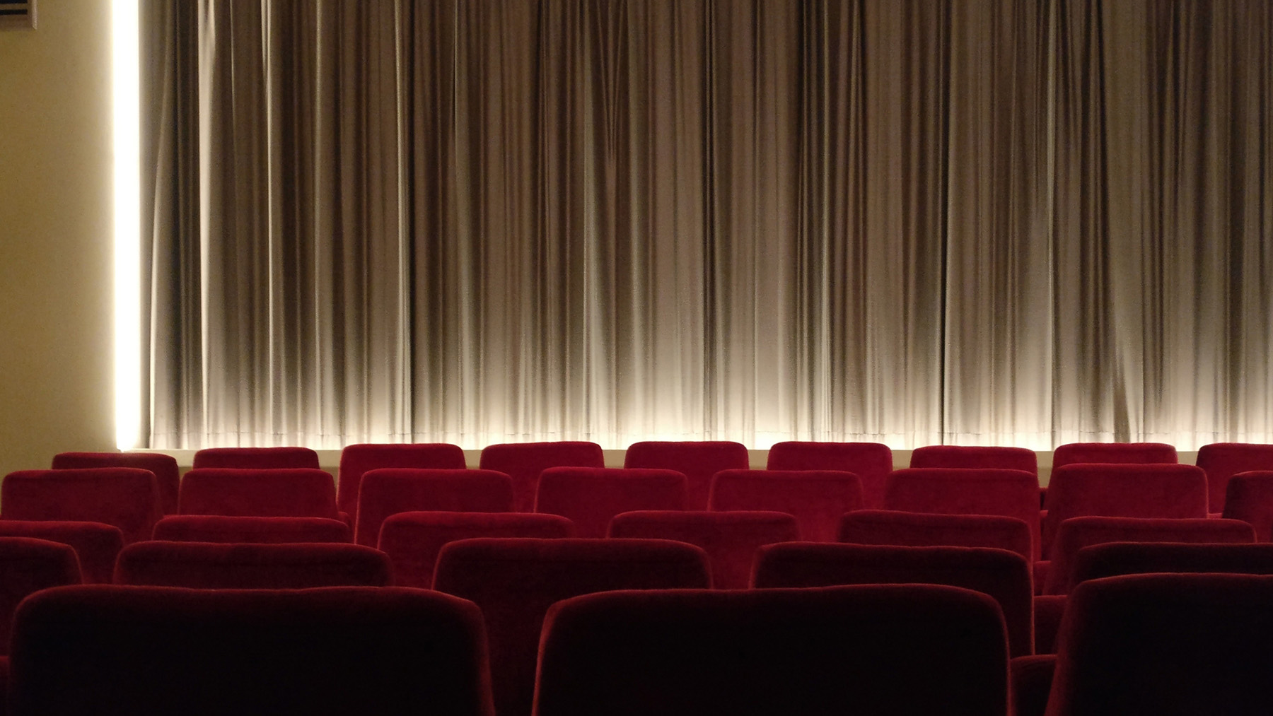 Stock image of a movie theater with lights on stage and empty red seats from RawPixel.com